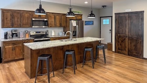 A kitchen with wooden cabinets, stainless steel appliances, a granite countertop, and bar stools. - Walk to Gull Lake! Spacious Family Home w/ Deck (Nisswa)