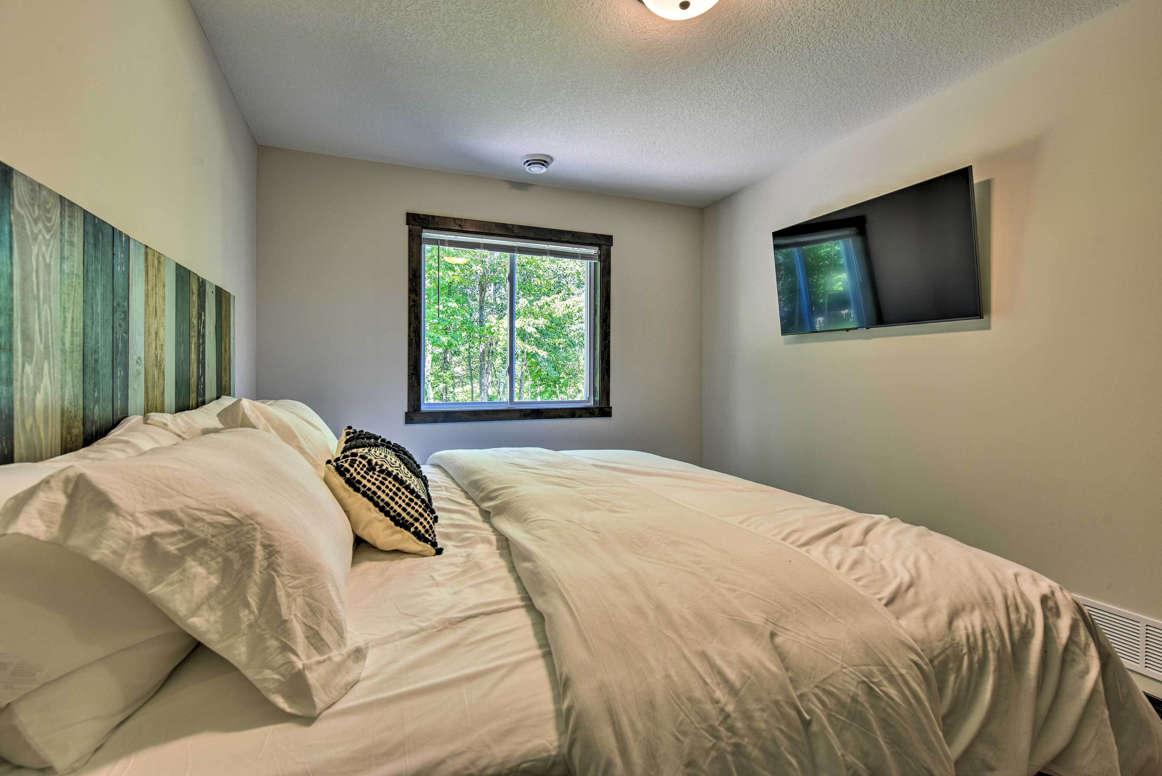 Ein Schlafzimmer mit Bett, Fenster und einem an der Wand montierten Fernseher.