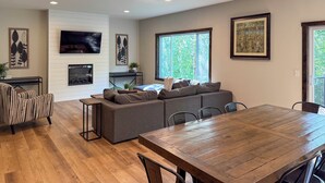 A modern living room with a wooden dining table, grey sectional sofa, and a flat-screen TV mounted on a white wall. - Walk to Gull Lake! Spacious Family Home w/ Deck (Nisswa)