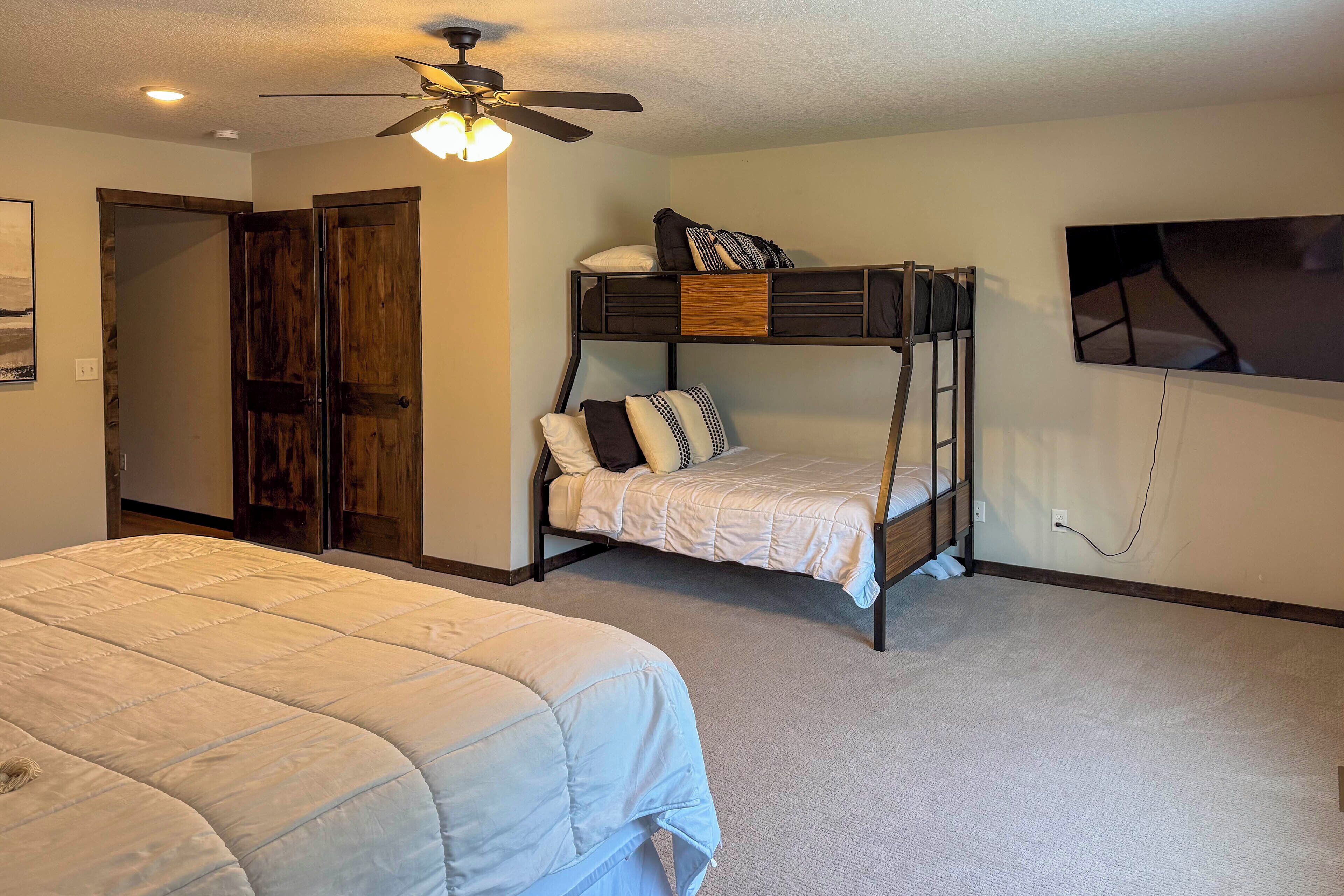 A room with bunk beds, a ceiling fan, a TV, and a door leading to another room.
