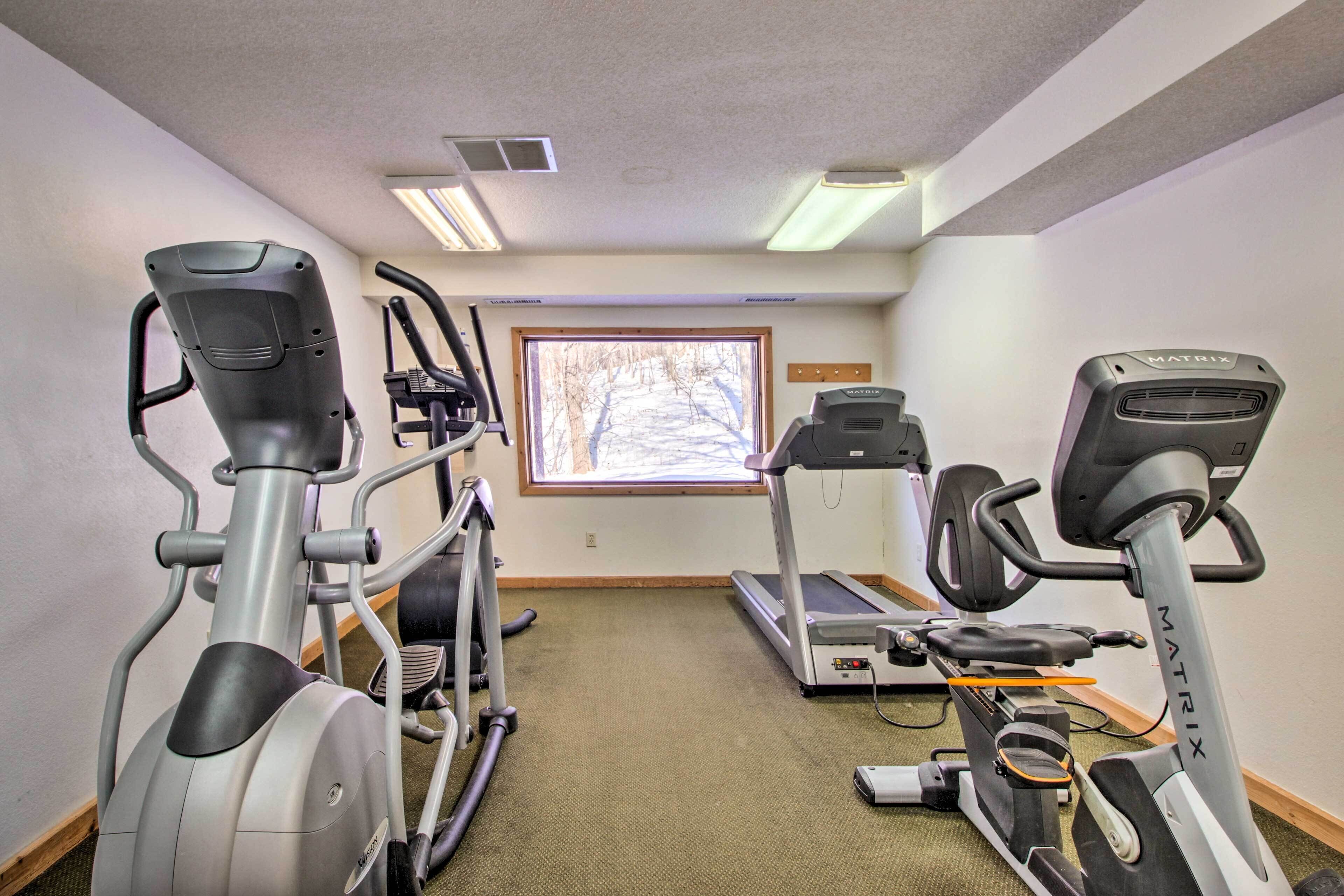 Un gimnasio con cintas de correr, elípticas y un ventanal con vista a árboles.