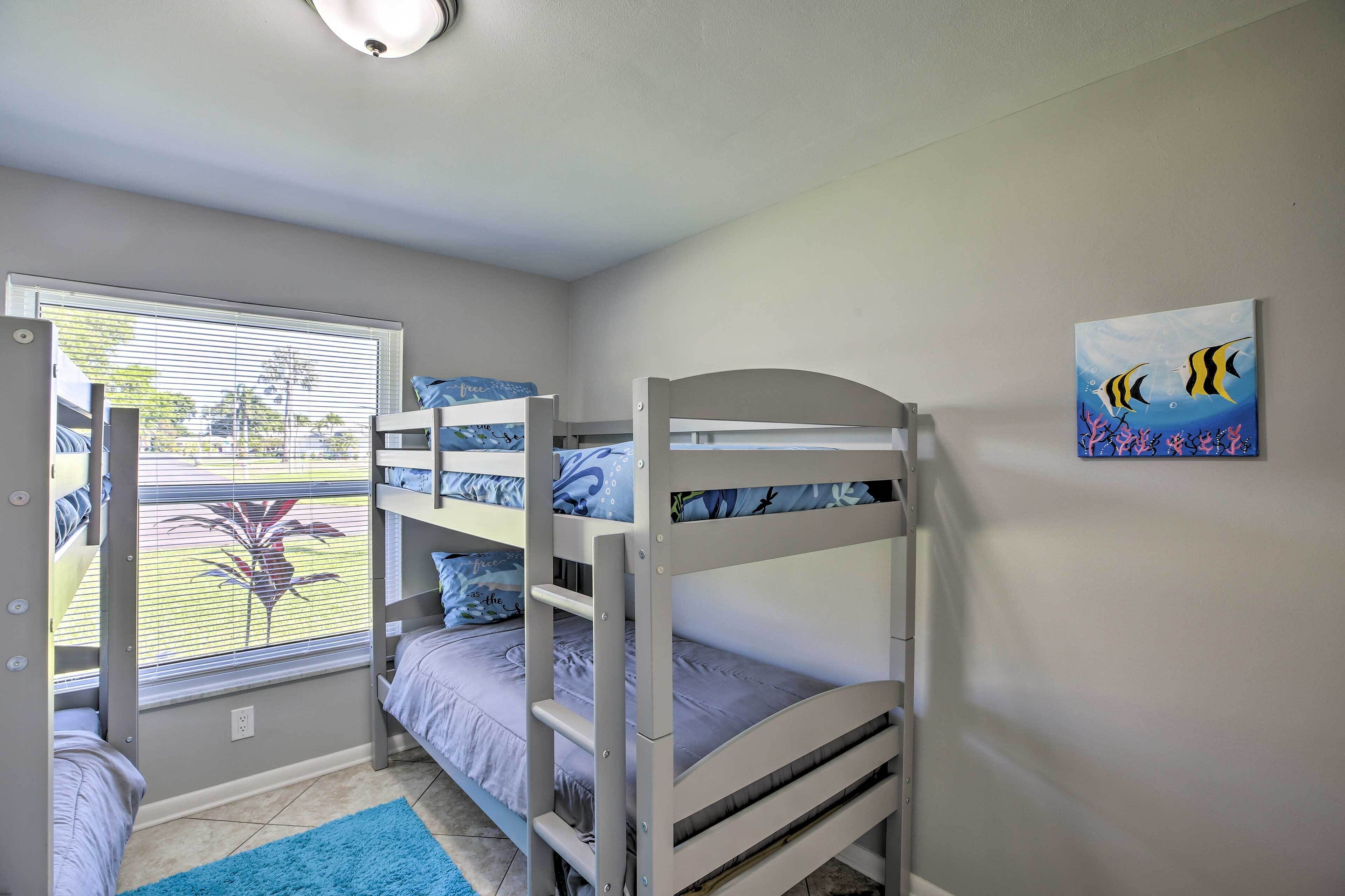 Een slaapkamer met een stapelbed, een raam, een schilderij en een blauw vloerkleed.