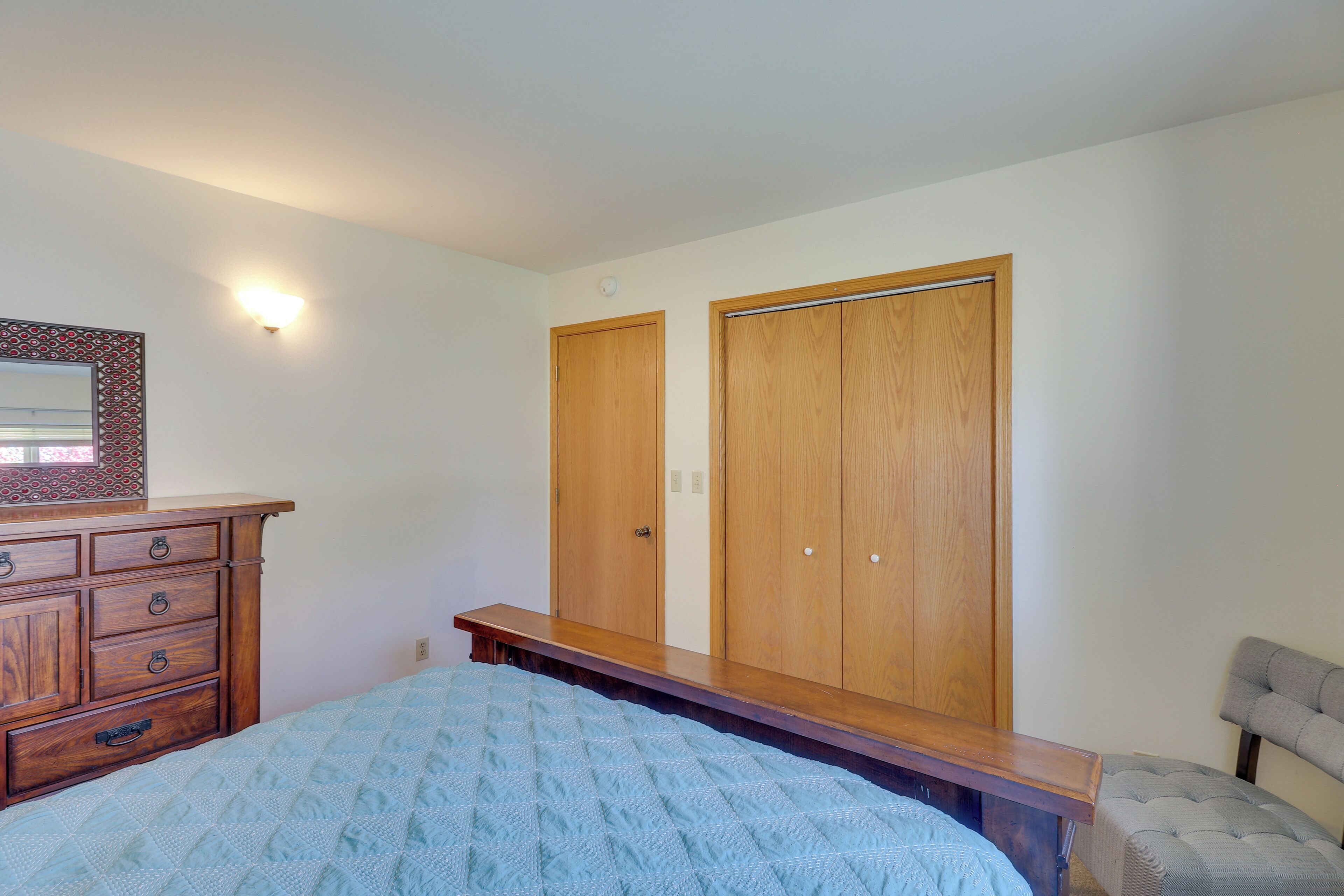 A bedroom with a bed, wooden wardrobe, dresser, bench, and a chair.