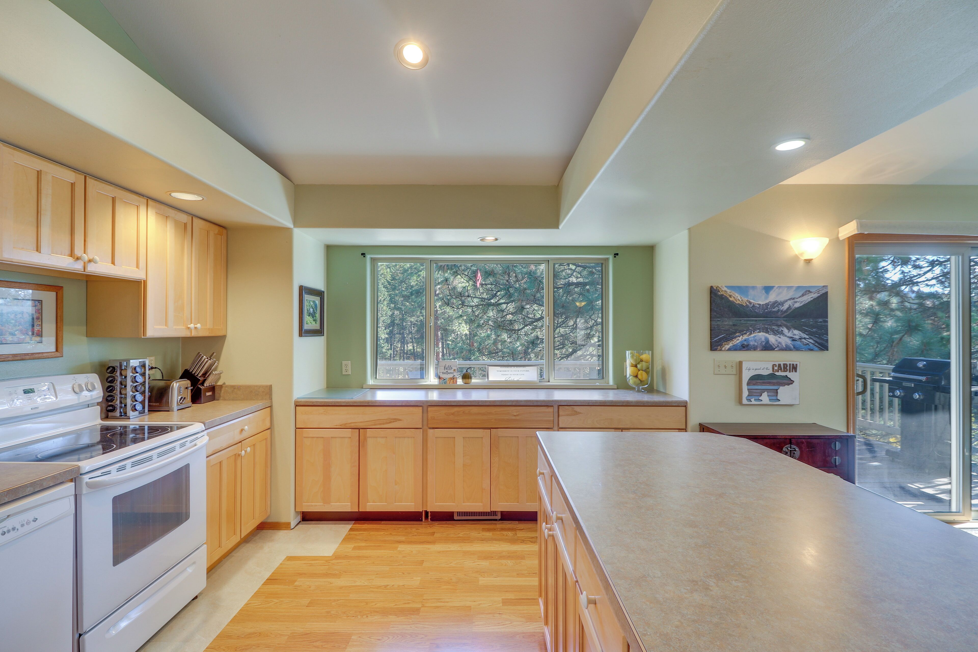 A modern kitchen with wooden cabinets, a large island, and a view through the window.