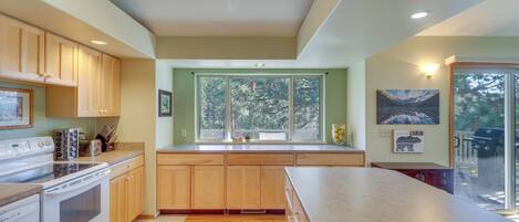 A modern kitchen with wooden cabinets, a large island, and a view through the window.