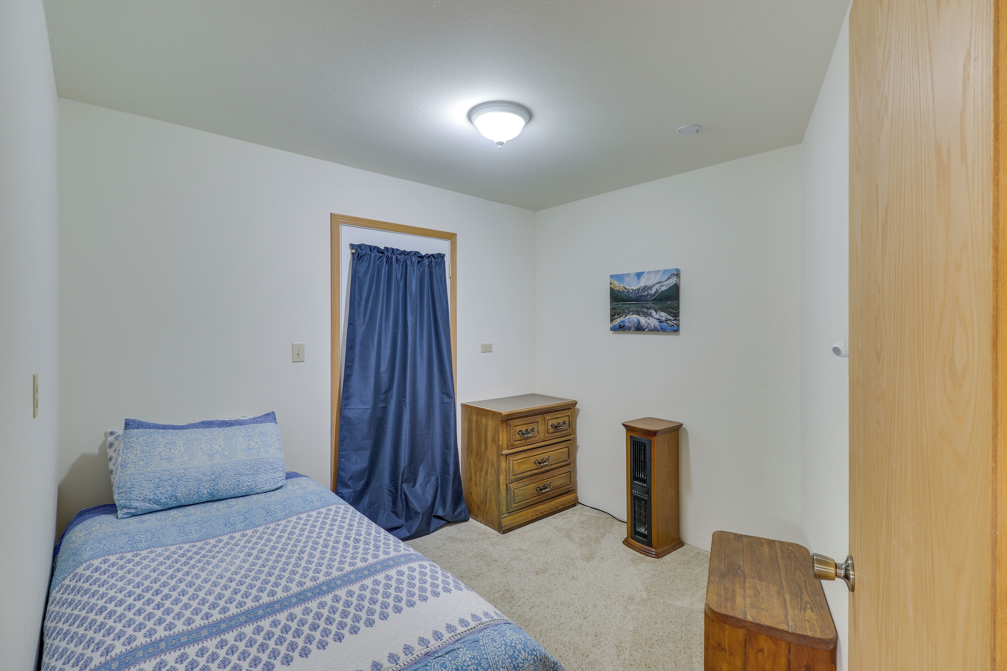 Une chambre à coucher comprenant un lit, une commode en bois, un petit meuble, une porte et un tableau accroché au mur.