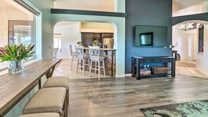 A spacious living area with a kitchen in the background, a dining table with chairs, and a TV mounted on the wall.