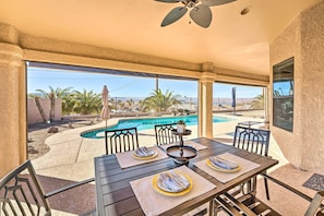 An outdoor patio with a pool, dining table set with plates, and chairs.