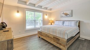 Une chambre à coucher avec un lit en bois, une fenêtre avec des stores, une lampe fixée au mur et un ventilateur de plafond.