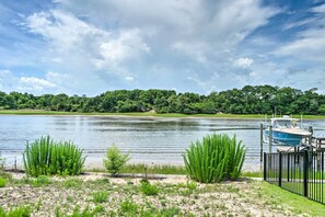 A serene lakeside view with a dock and boat, surrounded by lush greenery and a clear sky. - Modern Oak Island Escape: 1 Mile to Long Beach! (Oak Island)