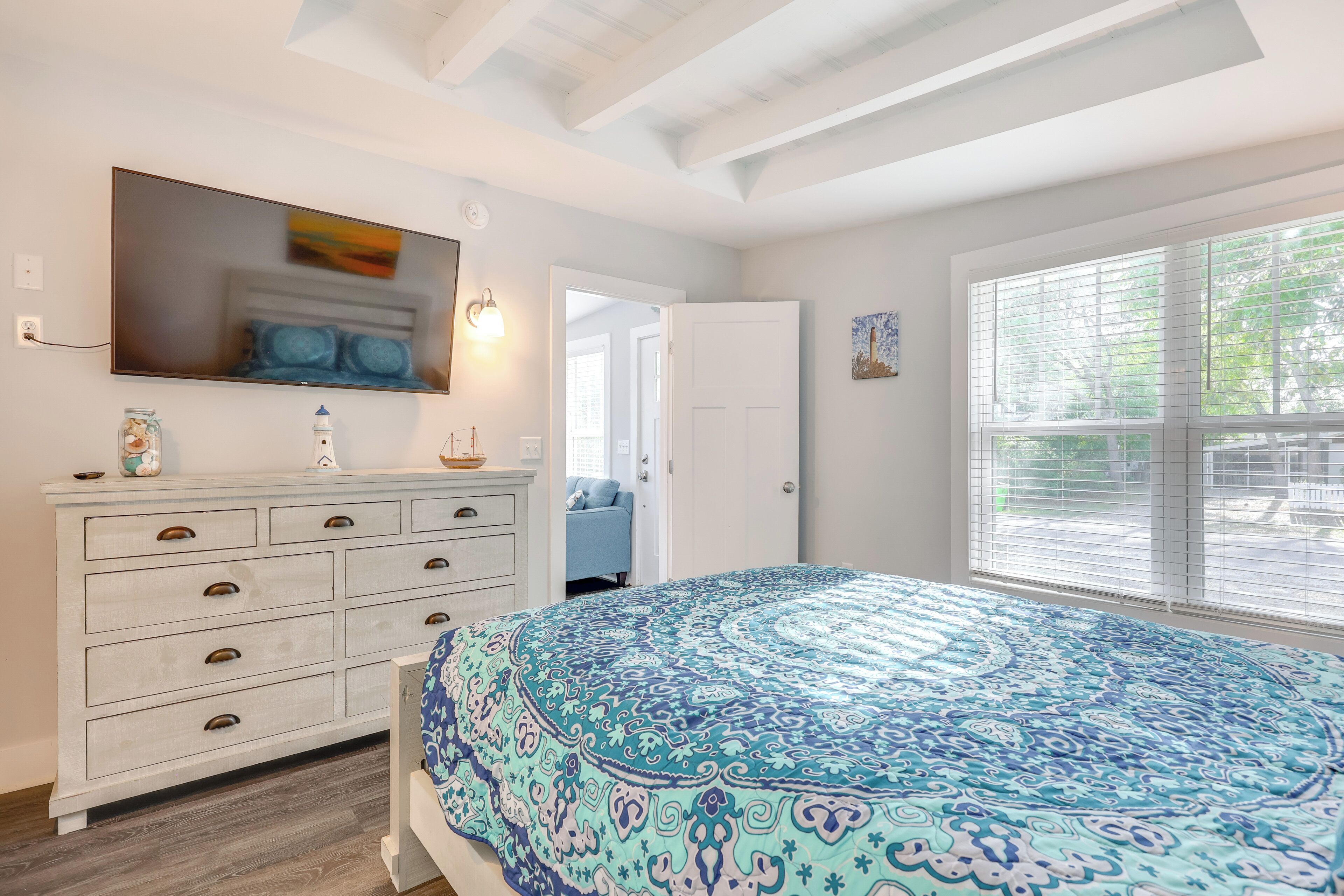 Une chambre avec un grand lit, une commode avec des tiroirs, un miroir et une fenêtre avec des stores.