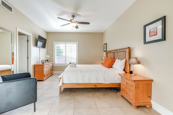 A bedroom with a bed, nightstands, a dresser, a ceiling fan, a TV, and a window with blinds.