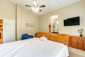 A hotel room with a bed, a wooden dresser, a television mounted on the wall, and a ceiling fan.