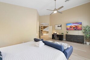 A bedroom with a bed, a desk, a chair, a television, and a ceiling fan.