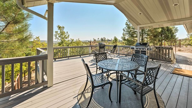 Eine überdachte Terrasse im Freien mit einem runden Tisch und Stühlen, einem Grill und Blick auf die umliegende Landschaft.