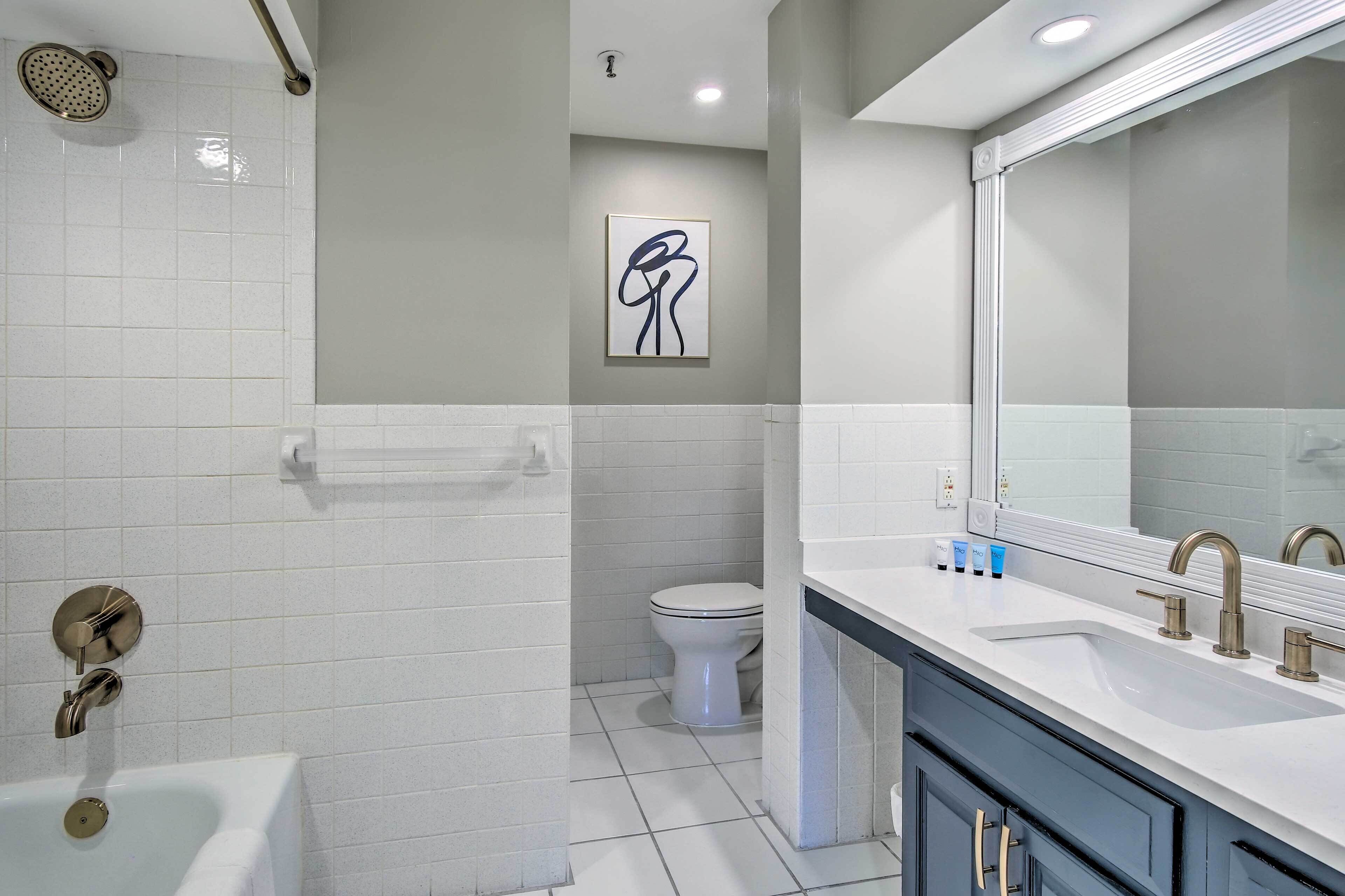 A modern bathroom with a bathtub, a toilet, and a sink with a large mirror.