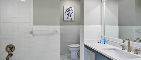 A modern bathroom with a bathtub, a toilet, and a sink with a large mirror.
