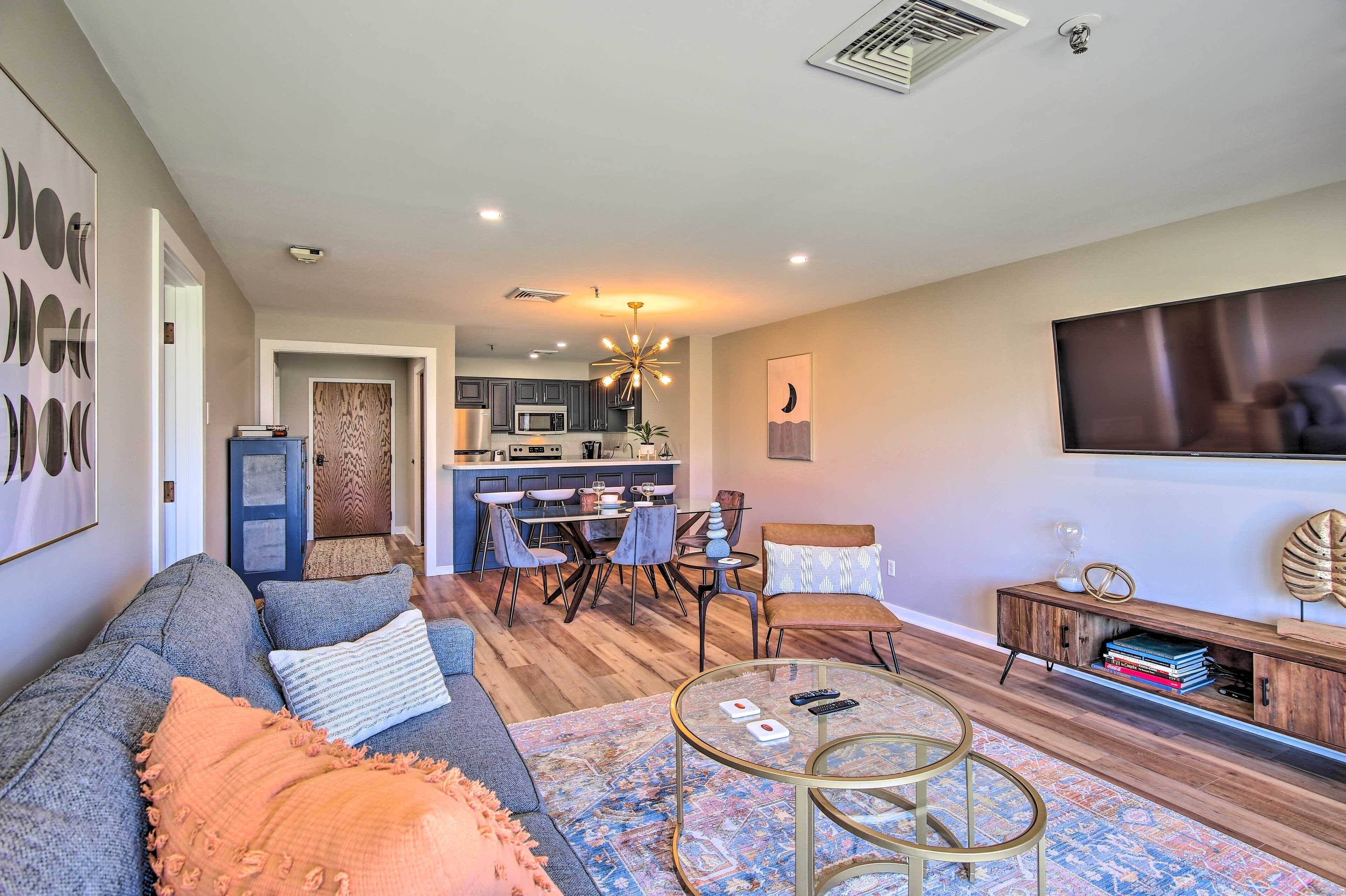 A modern living room with a sofa, coffee table, and a dining area with chairs and a kitchen in the background.