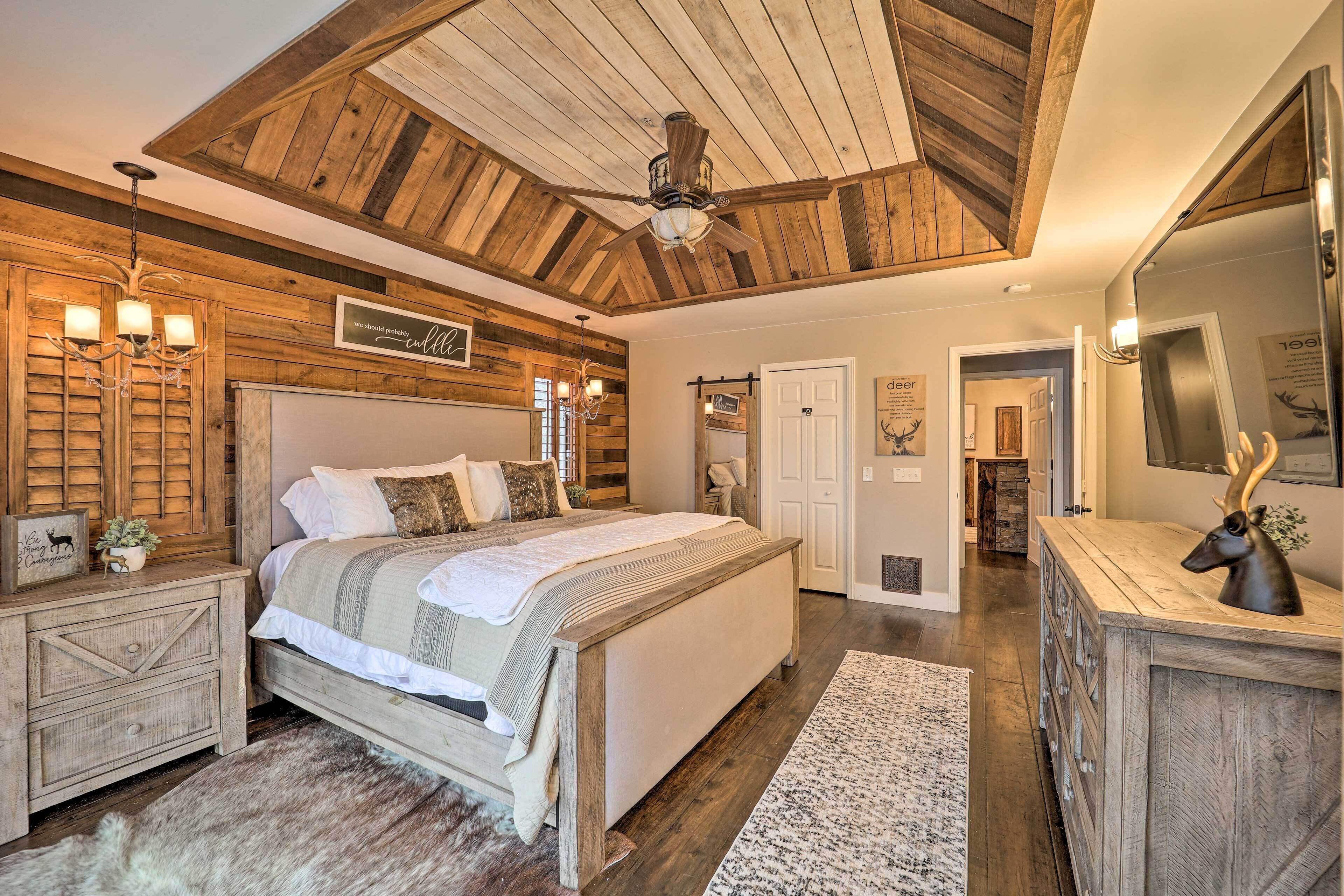 Quarto com teto de madeira, cama com cabeceira, mesa de cabeceira, penteadeira e espelho.