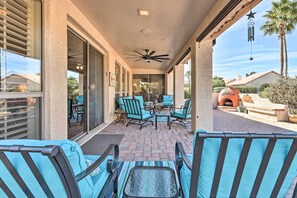 Eine überdachte Terrasse mit Gartenmöbeln, einem Deckenventilator und Blick auf den Garten.