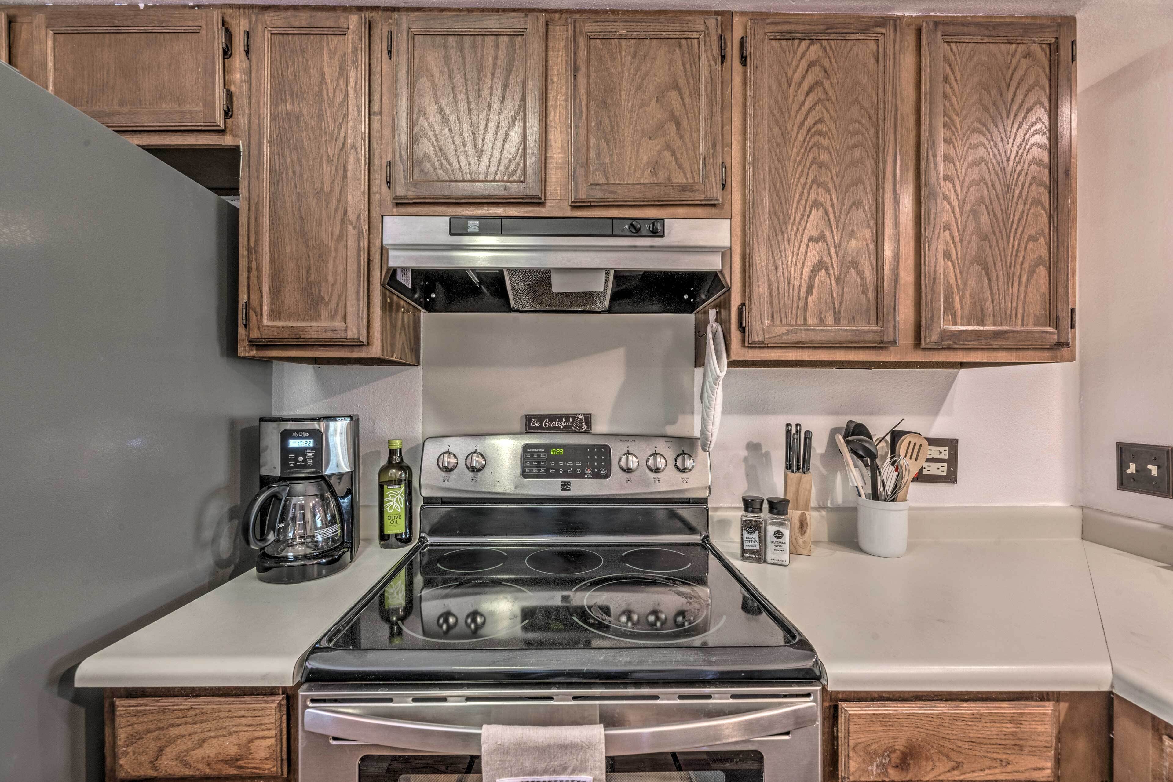 A kitchen with wooden cabinets, a stainless steel stove, a coffee maker, and a bottle of olive oil.