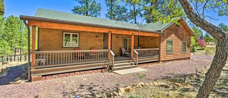 A rustic cabin with a porch, a small attached shed, and an American flag.