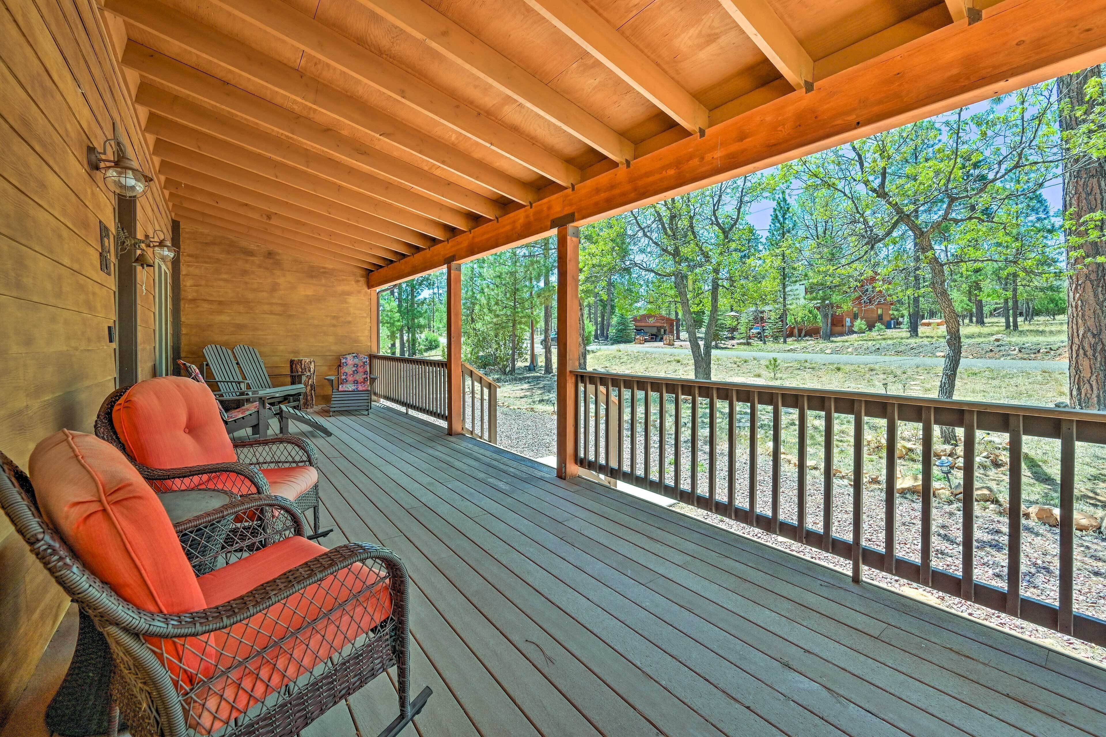 A covered porch with wicker chairs and a view of a forested area.