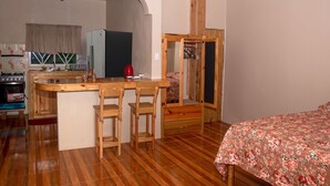 A compact room with a kitchenette, wooden furniture, and a bed with a floral bedspread.