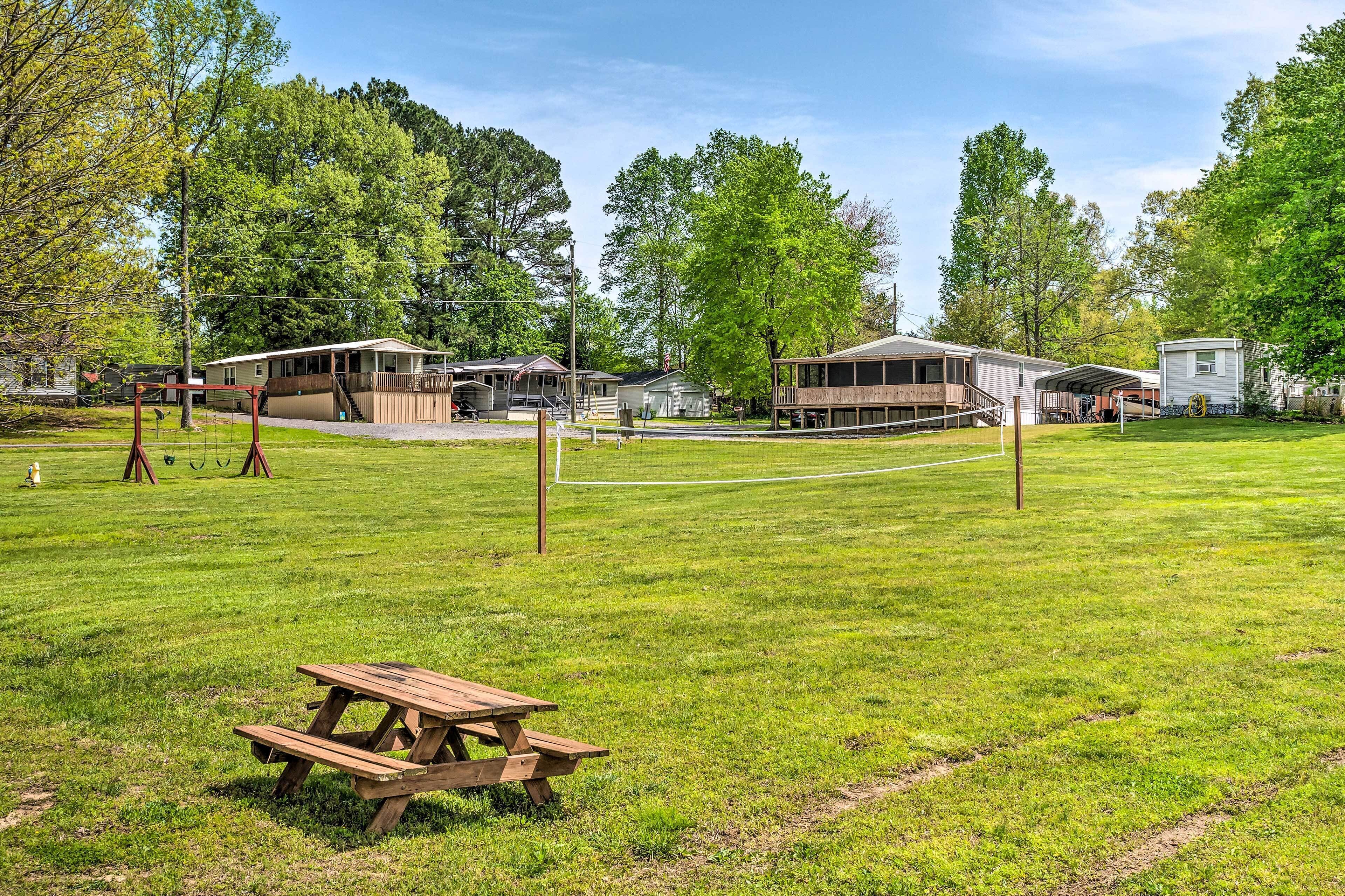 A grassy field with a picnic table, a volleyball net, and several cabins in the background.