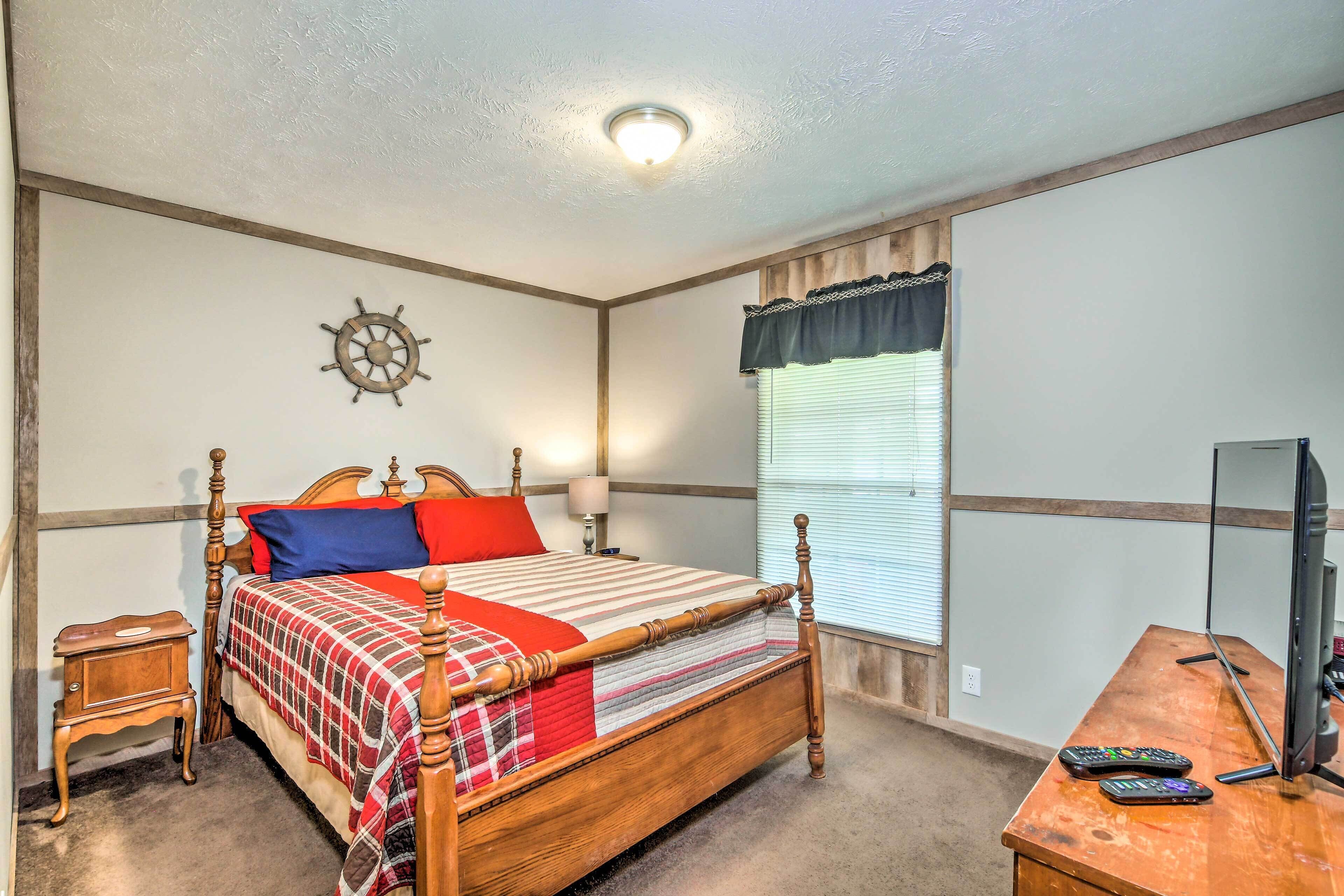 A bedroom with a wooden bed, a nightstand, a desk with a computer, and a window with blinds.
