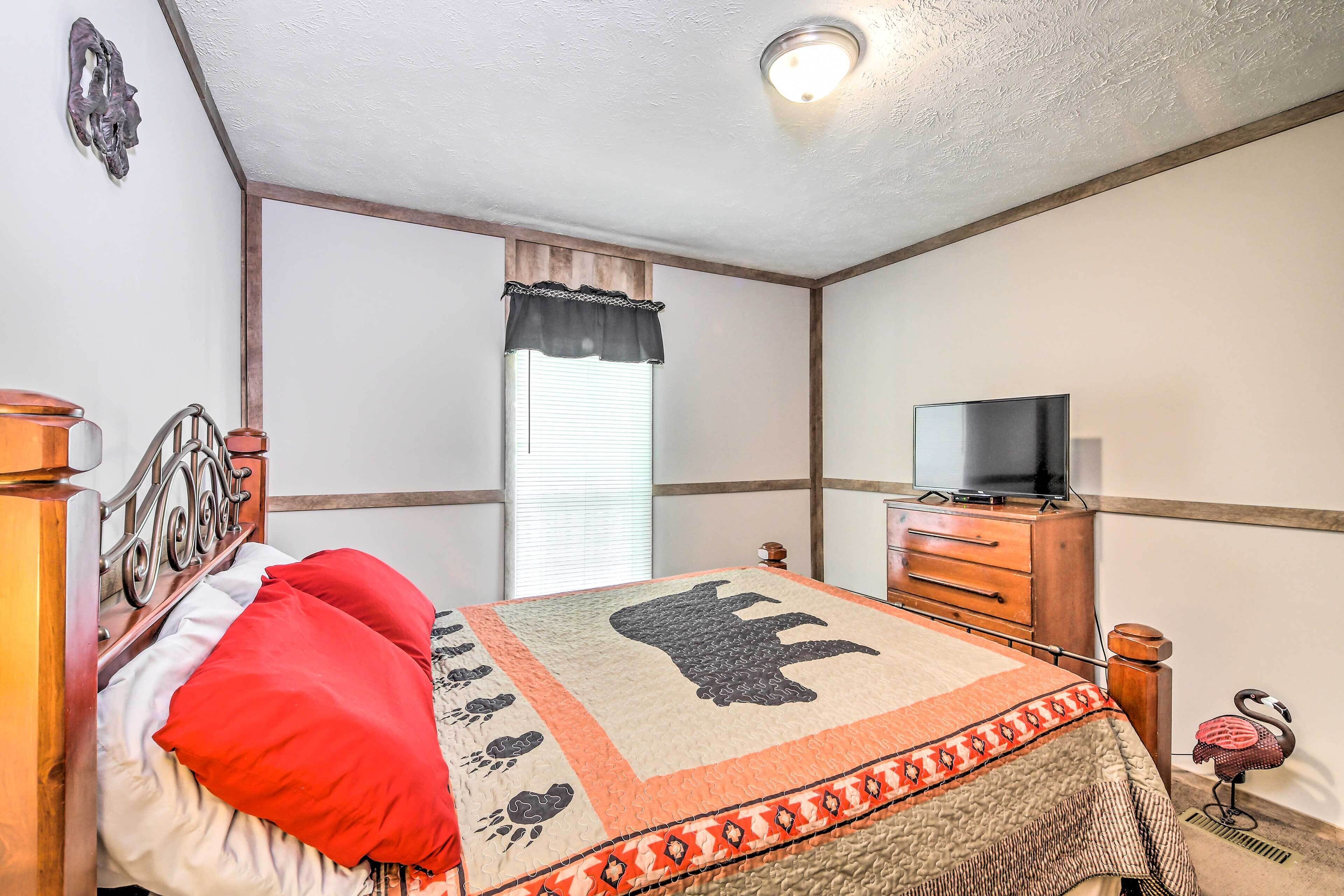 A bedroom with a bed, a dresser, a television, and a window with curtains.