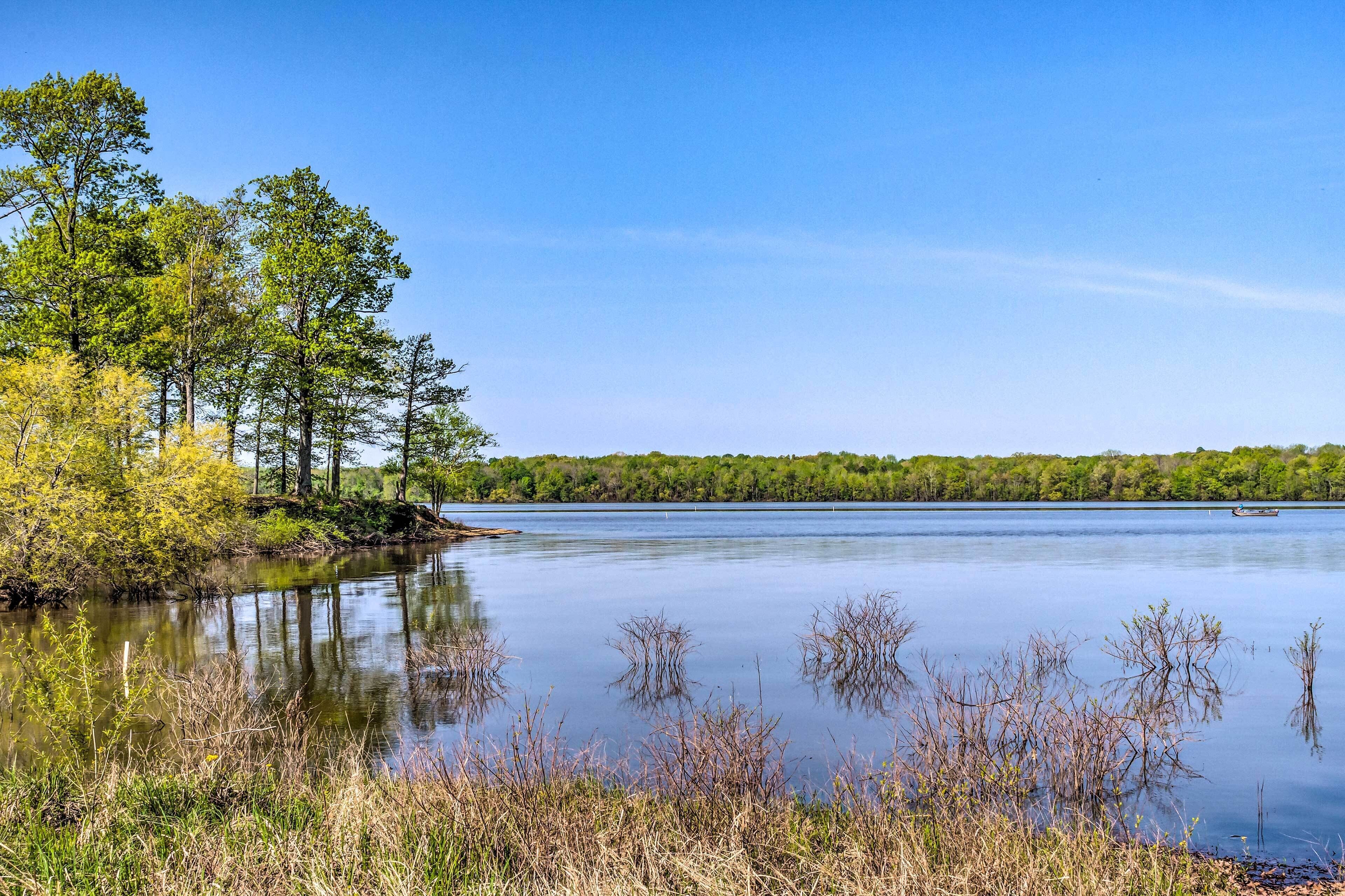 A calm lake with trees and a boat in the distance.