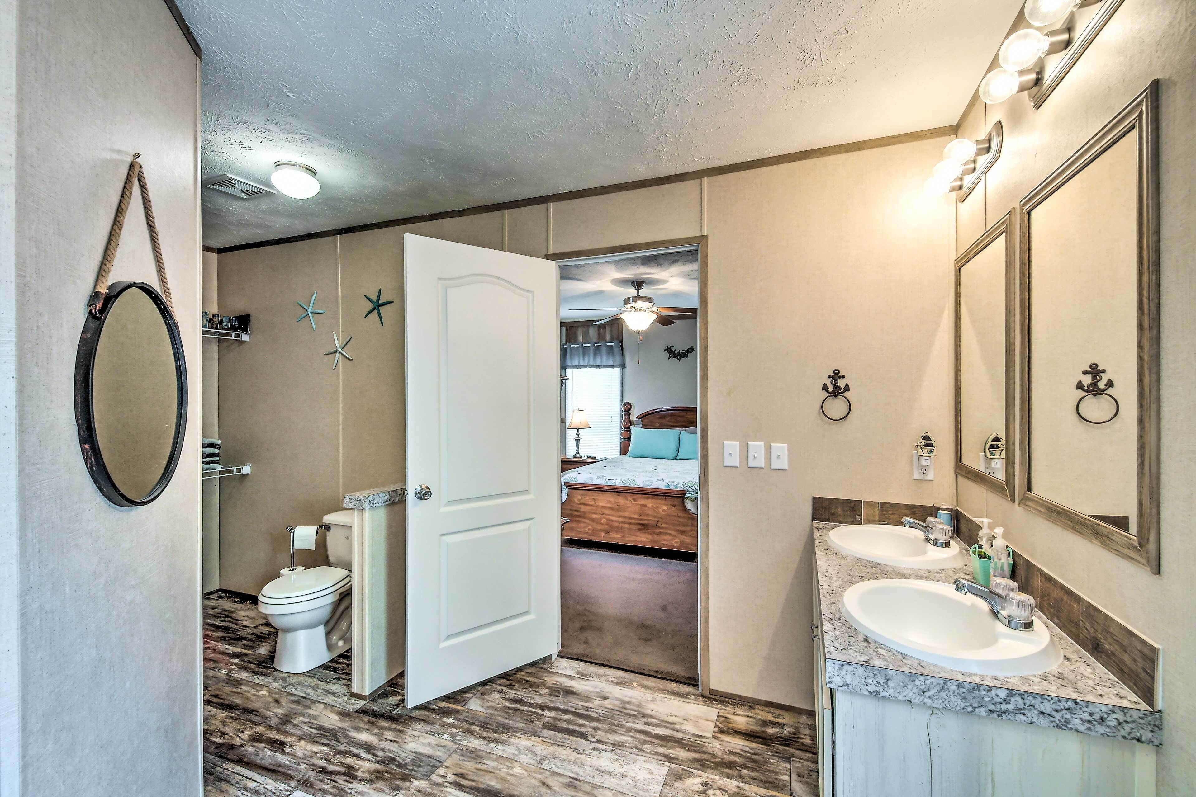 A bathroom with a double sink, a toilet, a mirror, and a ceiling fan.