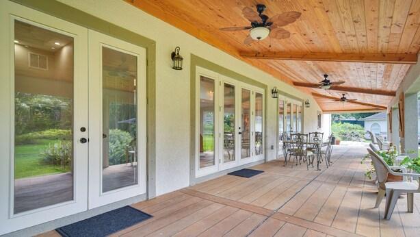 A covered patio with wooden flooring, glass doors leading to a garden, and outdoor furniture. - St Petersburg Getaway - 5 Mi to Tropicana Field! (St. Petersburg)