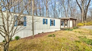 A mobile home with a small porch and a garage, surrounded by trees and a grassy area.