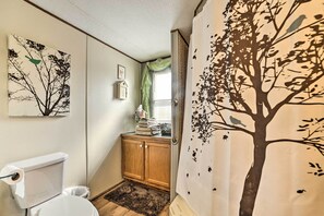 A bathroom with a toilet, a wooden cabinet, a rug, and a window with a view of trees and birds.
