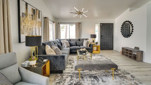 Un salon moderne avec un canapé d’angle gris, un lampadaire noir et doré, et un tapis noir et blanc.