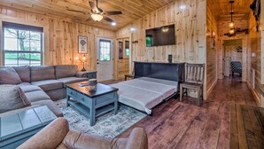A cozy cabin interior with a large bed, a sofa, a coffee table, and a TV mounted on the wall.