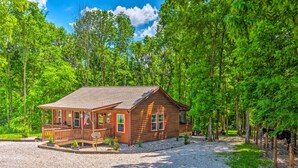 A wooden cabin with a porch, surrounded by trees and gravel.