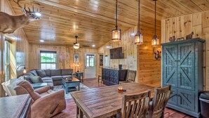A rustic interior with a wooden ceiling, a mounted deer head, a wooden dining table, and a cozy seating area.