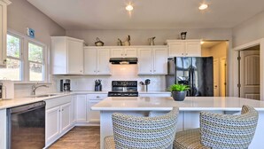 A modern kitchen with white cabinetry, a central island, and two patterned chairs. - Family Home w/ Views ~ 5 Mi to Downtown Asheville! (Asheville)