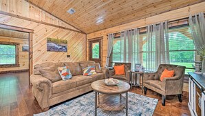 A cozy cabin interior with a wooden ceiling, a sofa, a chair, a small table, and a window with curtains. - Setting Sun Eagletown Gem: Real-log Cabin! (Eagletown)
