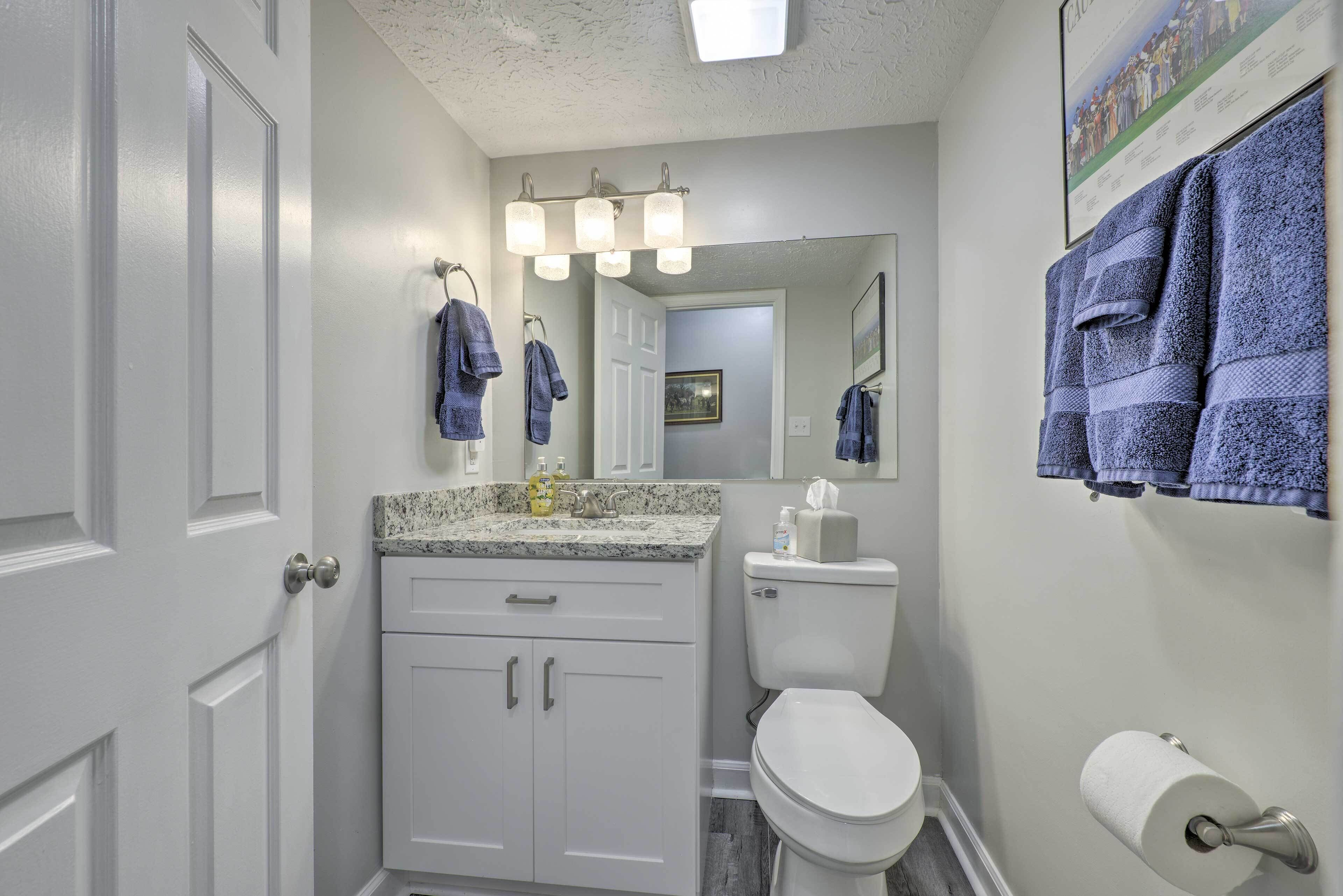A bathroom with white cabinets, a toilet, a sink with a granite countertop, and a mirror with a towel rack.