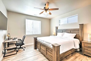 A bedroom with a wooden bed, a desk with a chair, a ceiling fan, and two bedside tables.