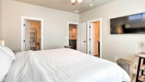 Ein Schlafzimmer mit Bett, Deckenventilator, an der Wand montiertem Fernseher und einem Kleiderschrank mit Tür zu einem Badezimmer.