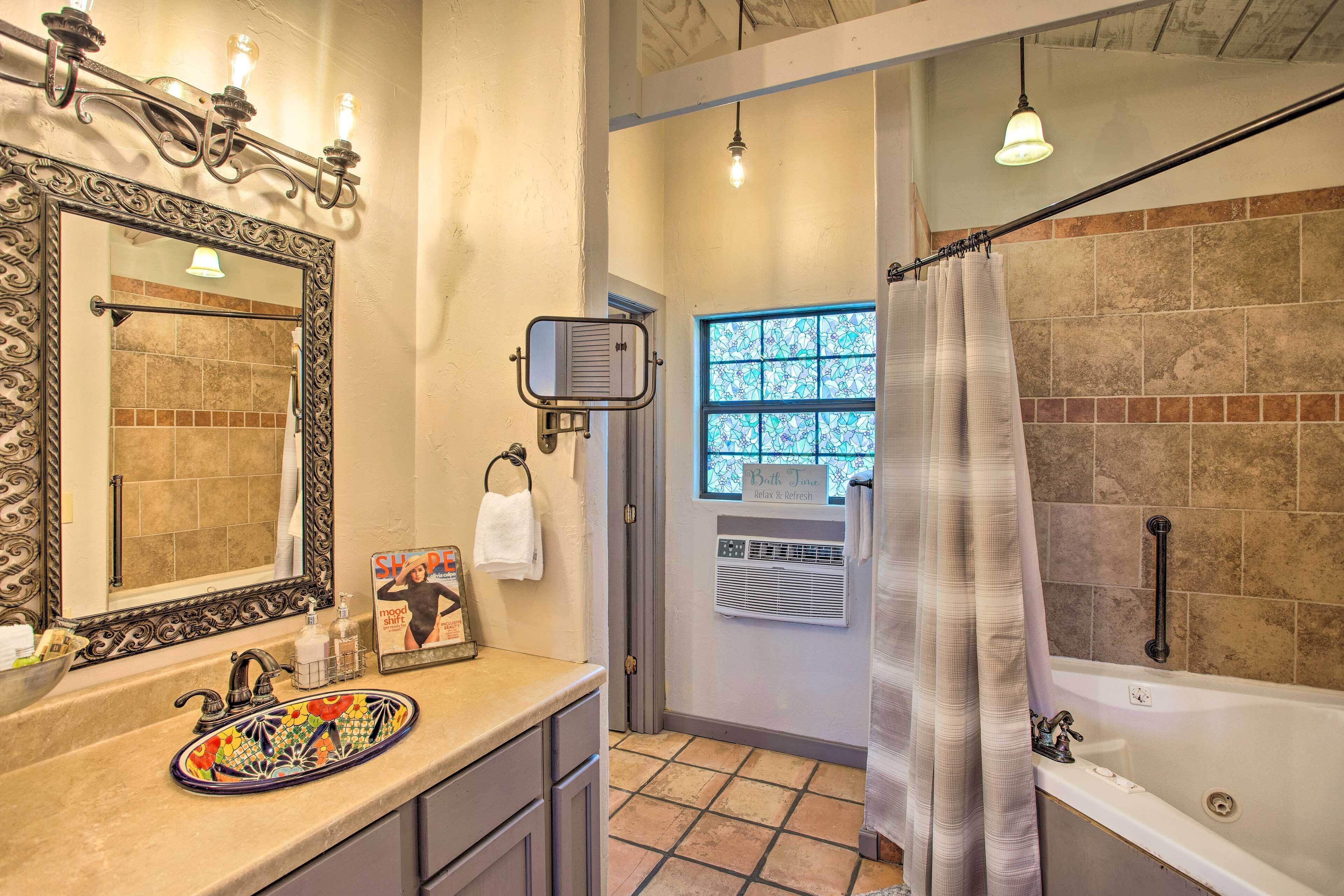 A bathroom with a large mirror, a colorful sink, a bathtub, and a shower curtain.