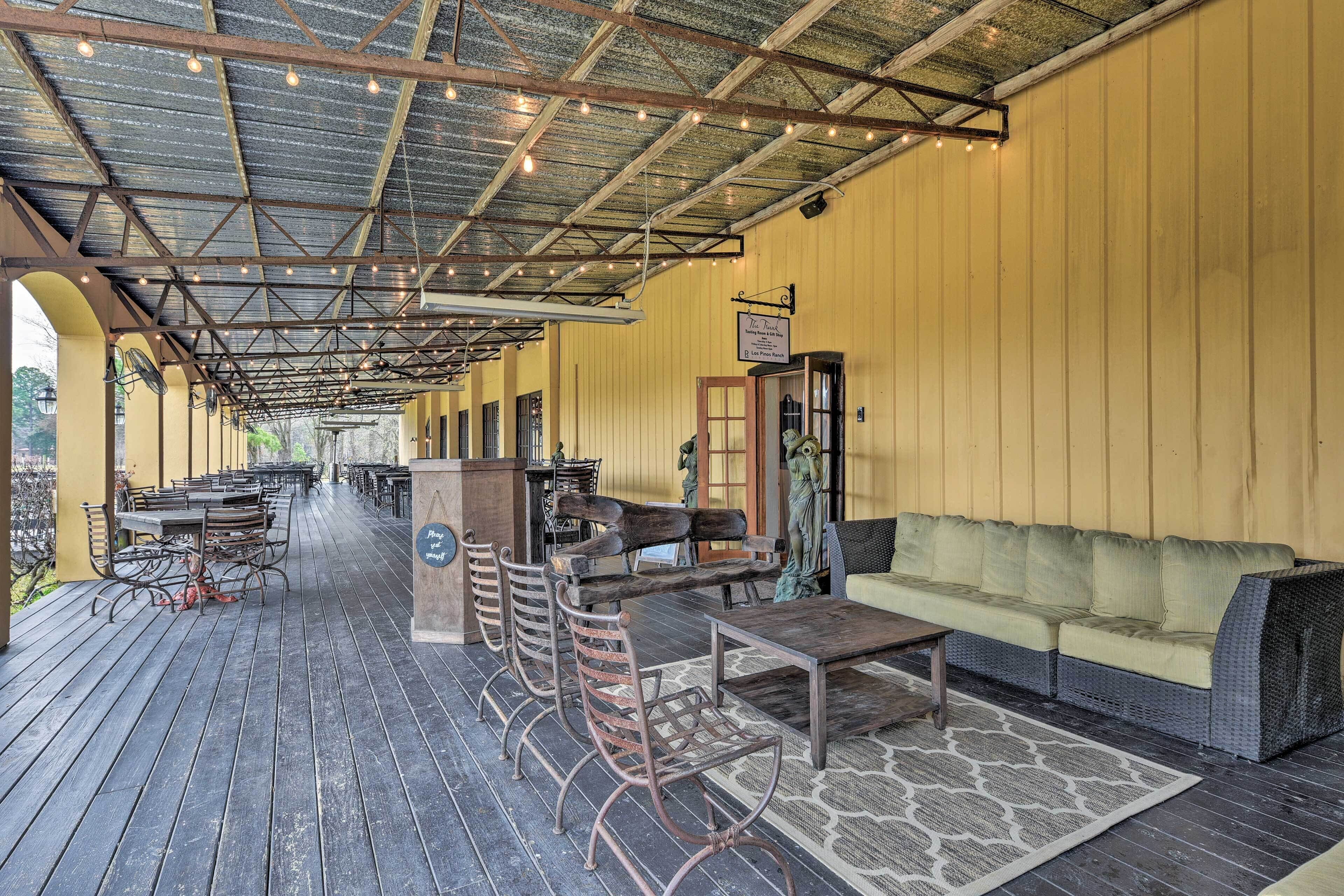 An outdoor patio area with wooden tables and chairs, a sofa, and a small bar area.