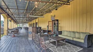 An outdoor patio area with wooden tables and chairs, a sofa, and a small bar area.