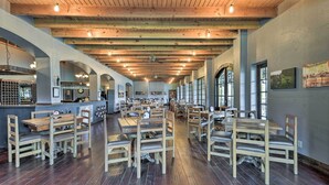 Un restaurante espacioso con mesas y sillas de madera, una zona de bar y amplios ventanales que dejan entrar luz natural.