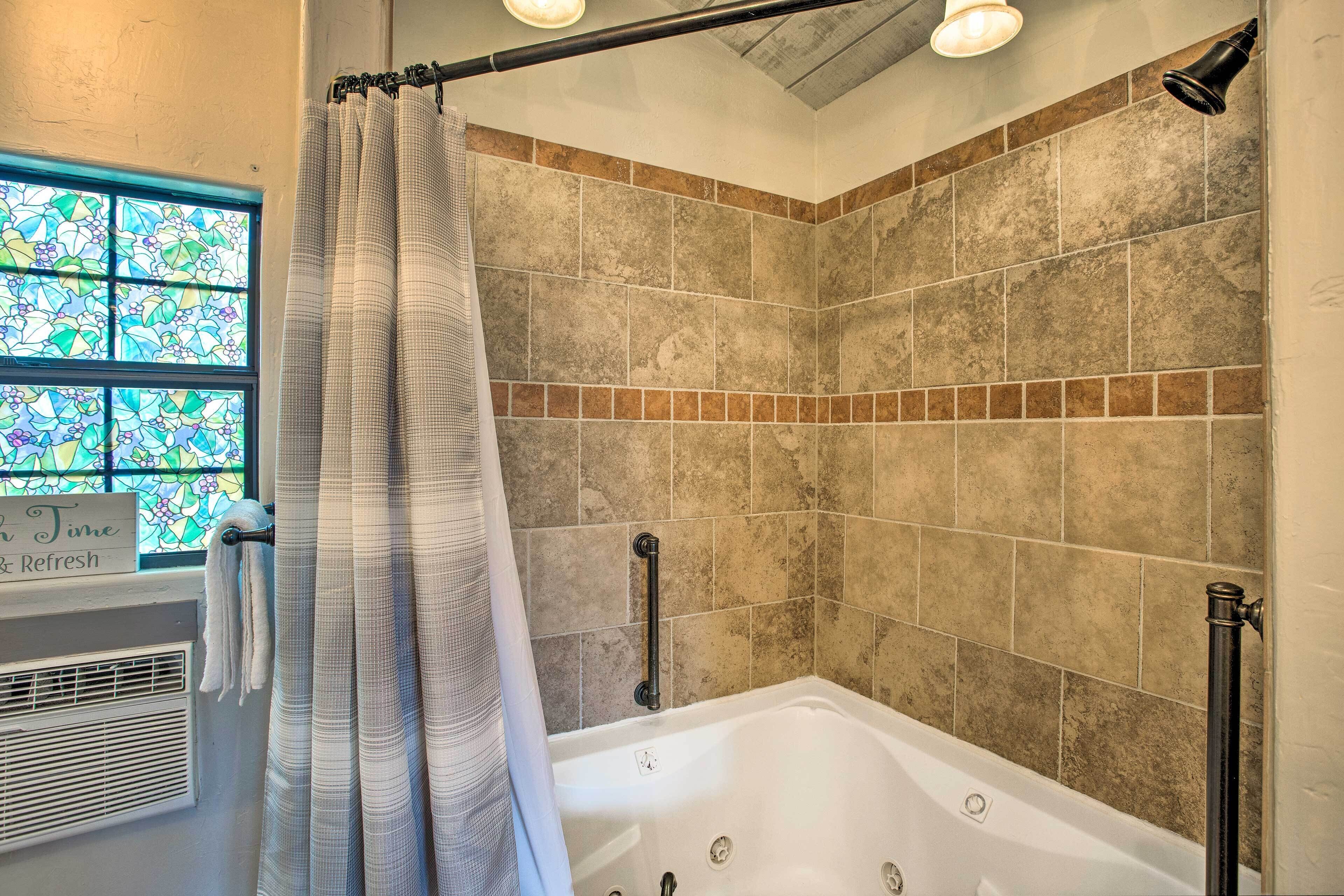 Une salle de bain équipée d’une baignoire, d’une douche et d’une fenêtre ornée de vitraux.